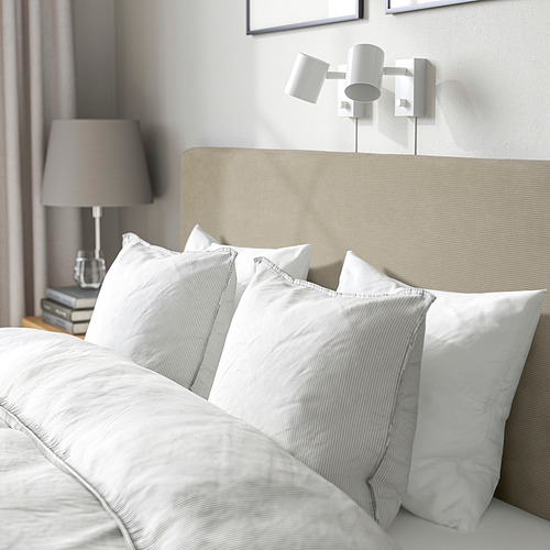 Acogedora cama con cabecera acolchada, almohadas cuidadosamente dispuestas y lámparas integradas para la lectura nocturna.