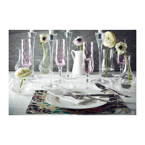 Elegante mesa con vajilla blanca OFANTLIGT, cristalería transparente y manteles individuales florales rosas. Flores individuales en jarrones pequeños.