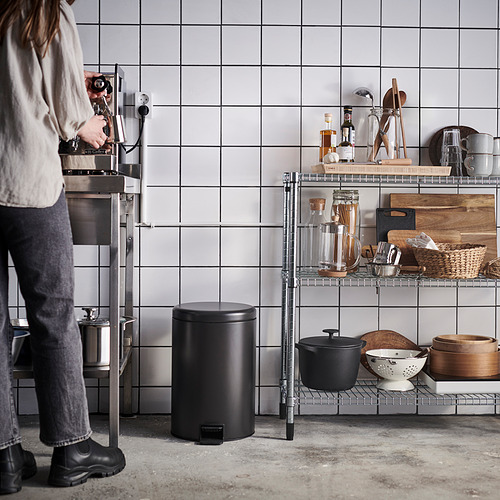 Persona que opera una máquina de café en una cocina moderna con contenedores negros y estantes que contienen varios artículos de cocina.