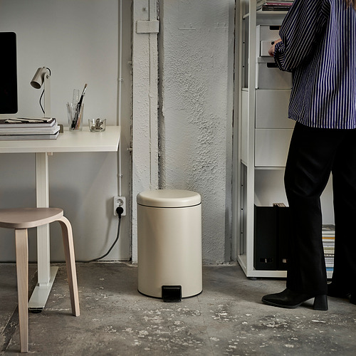 Persona parada cerca de un bote de basura y un escritorio con una computadora y libros.