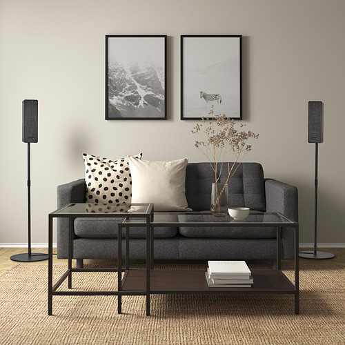 Sala de estar moderna con sofá gris, mesa, fotos de pared, altavoces y decoración.
