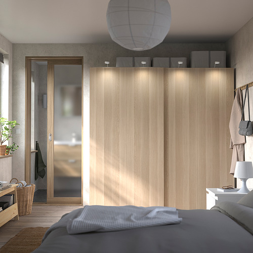 Un dormitorio minimalista con armario PAX de madera clara, puertas correderas e iluminación integrada.