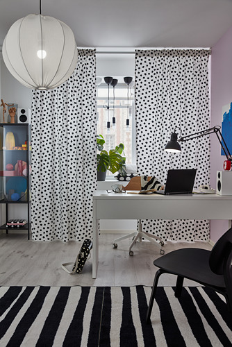 Moderna oficina en casa con escritorio blanco MICKE, silla negra, alfombra a rayas, cortinas de lunares y lámparas colgantes.