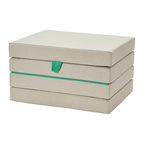 Un colchón de suelo plegable SLÄKT beige con ribetes verdes en una pila plegada. Es rectangular y está pensada para los niños.