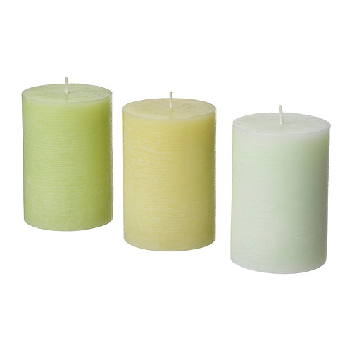 Tres velas cilíndricas en tonos verde, crema y blanco, cada una con una mecha en la parte superior, dispuestas en fila.