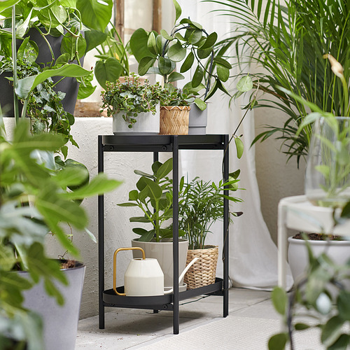 Soporte para plantas de metal negro con tres estantes que sostienen varias plantas verdes en macetas. Moderno y funcional expositor de jardín interior.