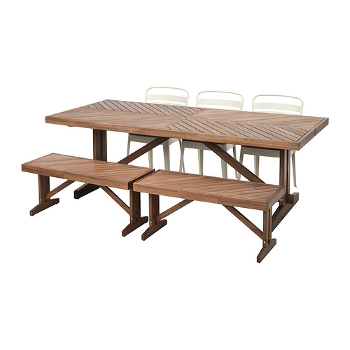 Una mesa de exterior de madera marrón con dos bancos a juego y cuatro sillas blancas.
