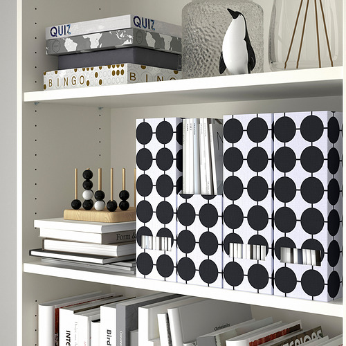 Estantería blanca con revisteros TJENA, juegos de mesa y artículos de decoración. Los soportes organizan papeles y revistas con un patrón elegante.