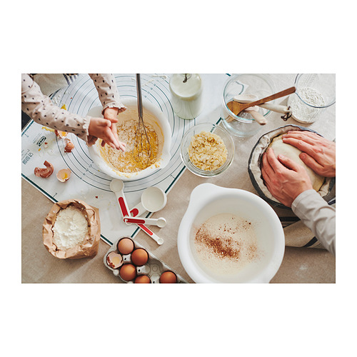 Escena de cocina ocupada con gente horneando, usando tazones para mezclar y varios ingredientes en una encimera.