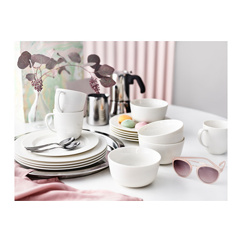 Vajilla de porcelana blanca con tazas, cuencos y platos sobre una mesa con detalles rosas, con elegantes líneas verticales y un diseño moderno.