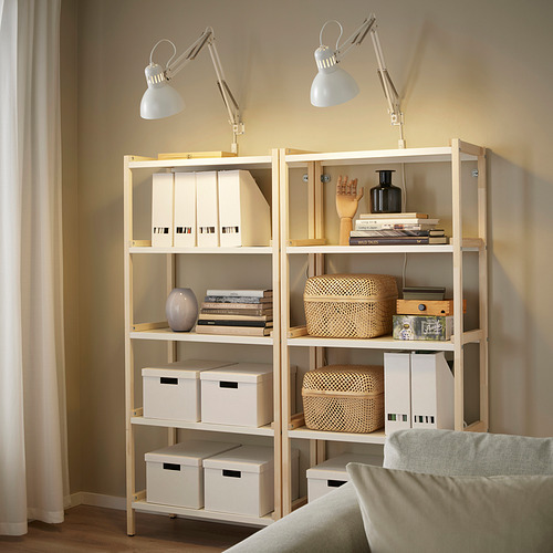 Dos lámparas TERCIAL en estanterías que iluminan libros y cajas junto a un sofá beige.