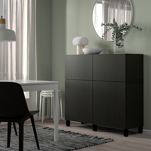 Sala de estar moderna con mueble negro BESTÅ, lámpara blanca, plantas y muebles minimalistas. Gran espejo sobre el armario.