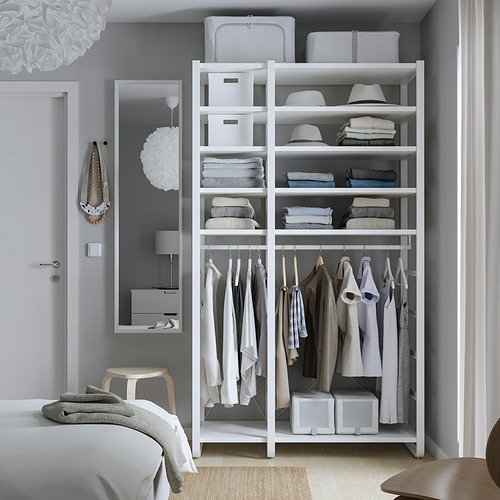 Dormitorio moderno con trastero blanco ELVARLI. Las estanterías de esquina guardan ropa y sombreros. Cuelga las prendas por debajo. Rodeado de cama y espejo.