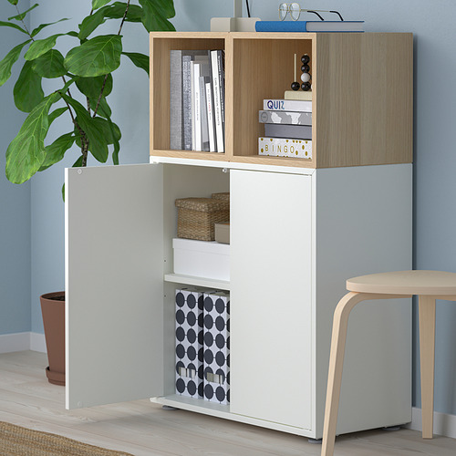 Mueble de almacenaje de madera y blanco con estantes abiertos y armarios cerrados. Contiene libros, cajas y una planta.