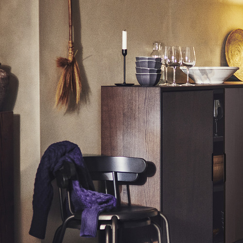 Un acogedor rincón de cocina con sillas negras cubiertas con telas azules, una vela y cuencos sobre una mesa de madera y decoración colgante.