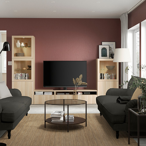 Sala de estar moderna con mueble de TV BESTÅ, mesa de centro de mármol oscuro y sofás negros contra la pared burdeos.