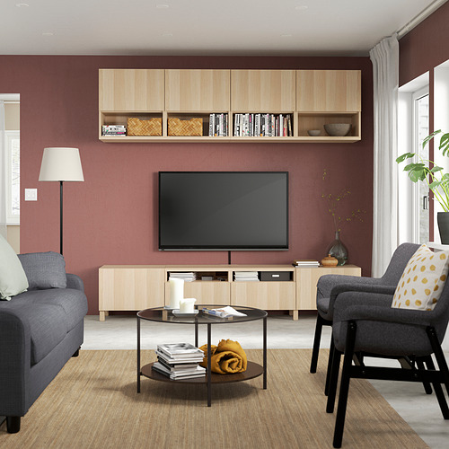 Salón moderno con BESTÅ, paredes burdeos, madera clara, muebles grises, mesa de centro con libros, y luz natural.