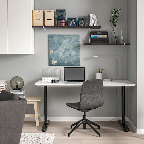 Oficina en casa moderna: escritorio BERGSHULT blanco, silla gris, estantes de pared con libros y computadora portátil.