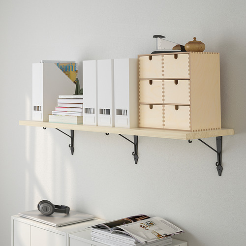 Estantería de pared de madera que contiene cajas y libros, con acabado en madera clara y soportes metálicos negros. Los elementos de exhibición incluyen auriculares y un jarrón.