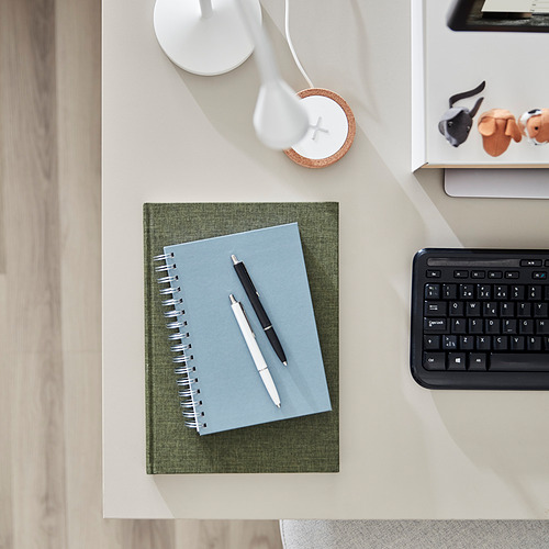 Una configuración de escritorio minimalista con un cuaderno verde, bolígrafos, teclado y lámpara, que enfatiza el tamaño y el diseño de los escritorios ROTTEN.