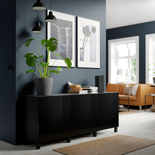 Habitación moderna con patas negras de STUBBARP debajo del aparador, planta de contención, arte enmarcado y libros. Silla de cuero naranja y alfombra beige cerca.