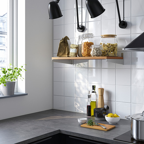 Cocina moderna con estantería, tarros y bolsas KUNGSFORS. Mostradores oscuros, hierbas, limones y lámparas negras.