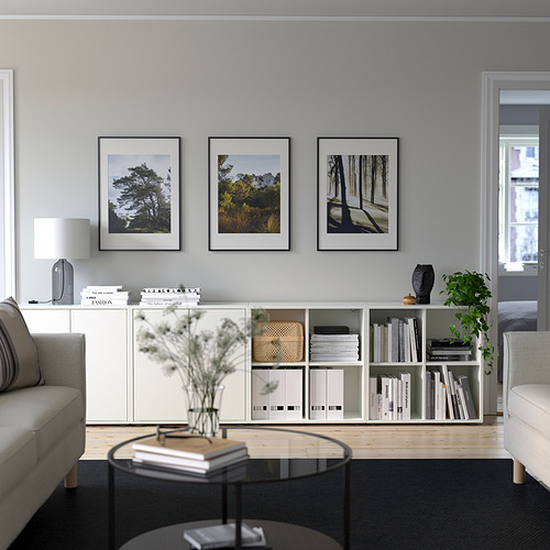 Salón minimalista con almacenaje EKET, libros, decoración, fotos de la naturaleza, mesa de centro redonda, sofá gris y luz natural.