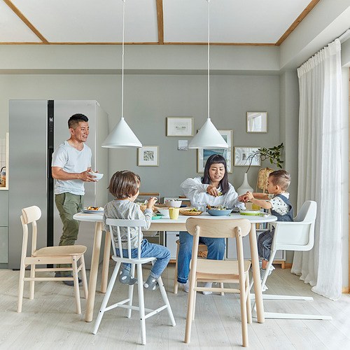 La familia disfruta de la comida con los niños sentados en coloridas sillas AGAM junior, diseñadas para la altura de la mesa de comedor, en una cocina acogedora.