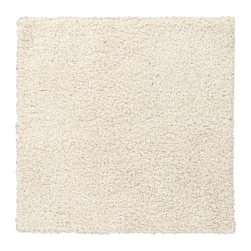 Una alfombra cuadrada blanca y suave con textura peluda, hecha de polipropileno y caucho sintético para una sensación cómoda.