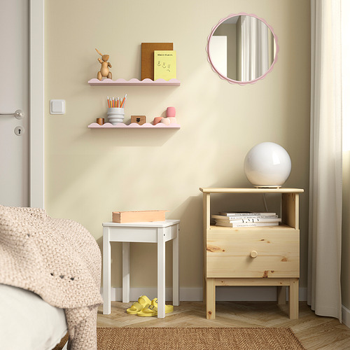 Pequeños estantes de pared rosa con varios artículos, junto a un cajón de madera y una lámpara de bola blanca.