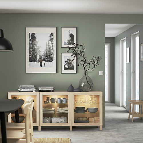 Comedor moderno con aparador BESTÅ en madera y cristal. Sostiene platos, decoración; Paredes verde salvia, arte, colgante negro.