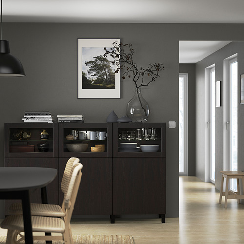 Aparador marrón oscuro BESTÅ con puertas de cristal, decoración de pared gris y zona de comedor.