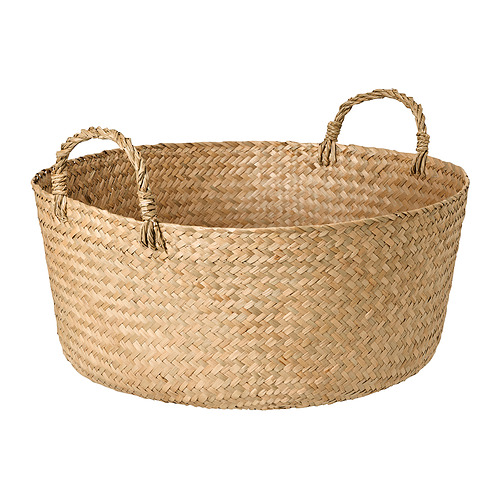 Una cesta tejida a mano por SANDJORD. Es de color beige, circular y hecho de material de juncia. Tiene dos asas para facilitar su transporte.
