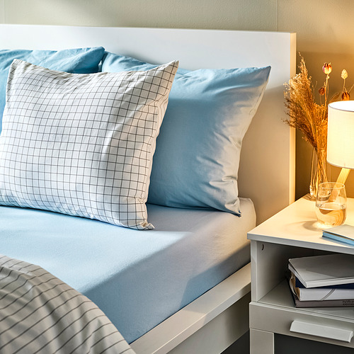 Cama con sábanas de algodón azul, lámpara, libros.