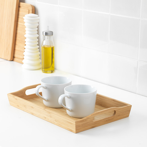 Dos tazas blancas en una bandeja de madera, con una botella de aceite amarillo y un salero blanco sobre una encimera de azulejos.