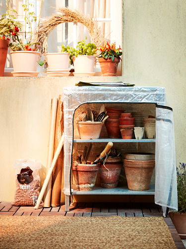 Pequeño almacenamiento en invernadero: unidad de acero plateado HYLLIS, cubierta transparente, macetas de terracota, plantas en balcón soleado.