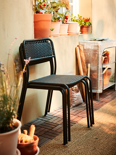 Silla de mimbre negro en el patio de baldosas con plantas en macetas, creando acogedores asientos al aire libre.