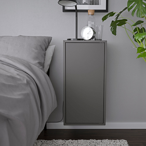 Moderno armario de pared gris, parte de una serie EKET de ikea, con un reloj y una lámpara, montado junto a una cama.