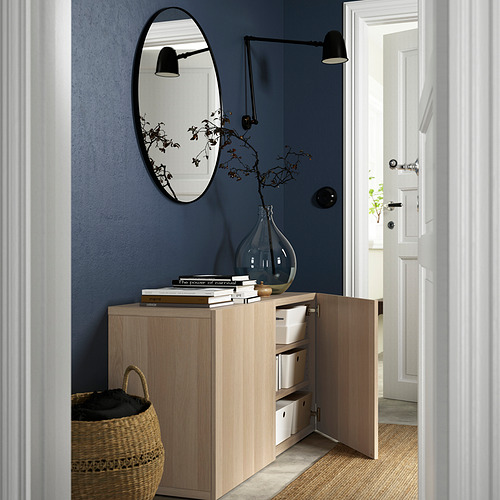 Aparador de madera con estantes ajustables y puertas de cierre suave, contra pared azul con espejo y lámpara.