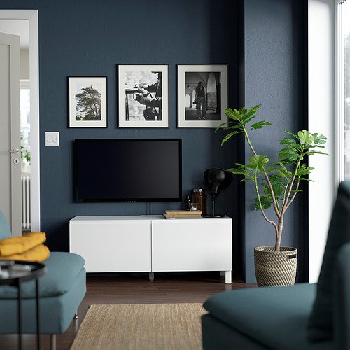 Sala de estar moderna con banco de tv BESTÅ, TV de pantalla plana, fotos, decoración, planta verde, sillas azules y almohada amarilla.