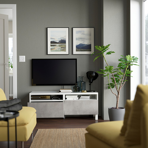 Moderno salón con banco de tv BESTÅ, cajones y gestión de cables entre sillas amarillas y una planta.