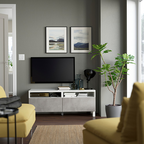 Sala de estar moderna con soporte de TV BESTÅ, televisor de pantalla plana negra, sillas amarillas, paredes grises y dos estampados de la naturaleza sobre el televisor.
