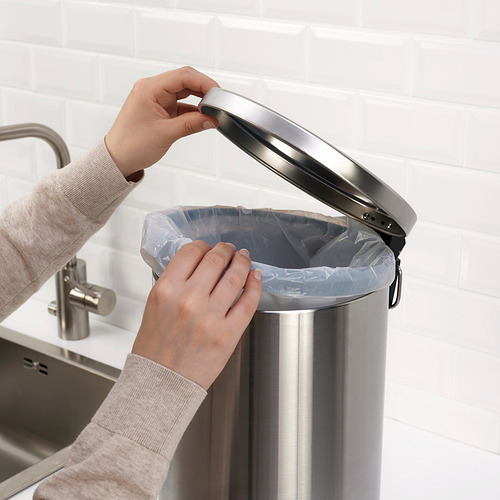 Persona colocando una bolsa de plástico dentro de un cubo de acero inoxidable con asa, apto para residuos o reciclaje en la cocina o el baño.