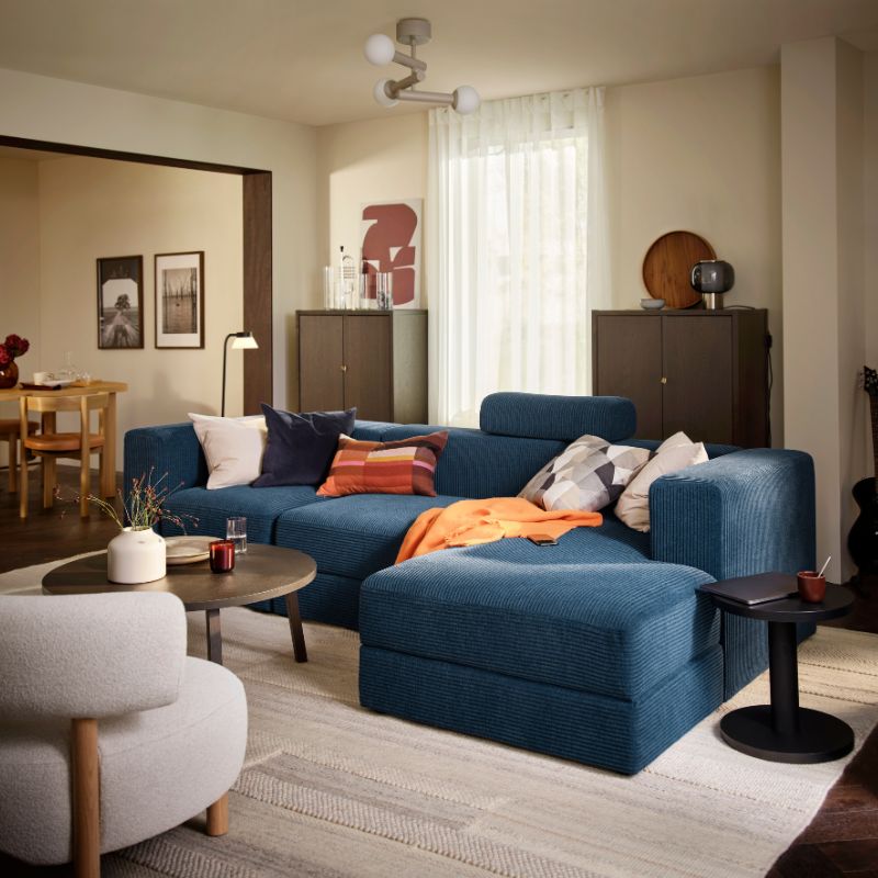A living room with a dark-blue JÄTTEBO four-seat sofa with chaise longue, complemented by a round table and decorative items.