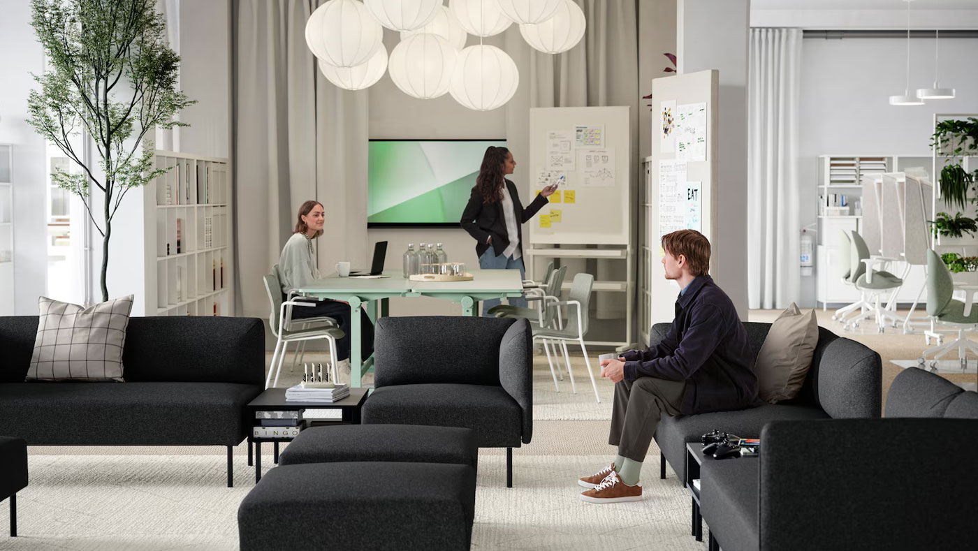 Large waiting room of a modern and creative office, in the background you can see a meeting table with someone exhibiting, the place looks spacious, bright and elegant.