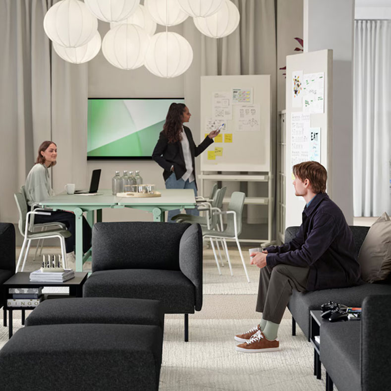 Large waiting room of a modern and creative office, in the background you can see a meeting table with someone exhibiting, the place looks spacious, bright and elegant.