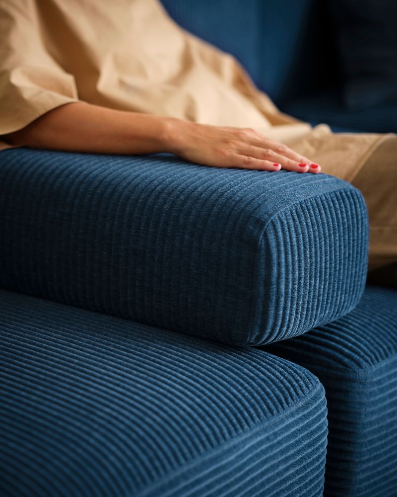 A person sits in a dark-blue JÄTTEBO four-seat modular sofa with their arm resting on a loose armrest placed in the sofa.