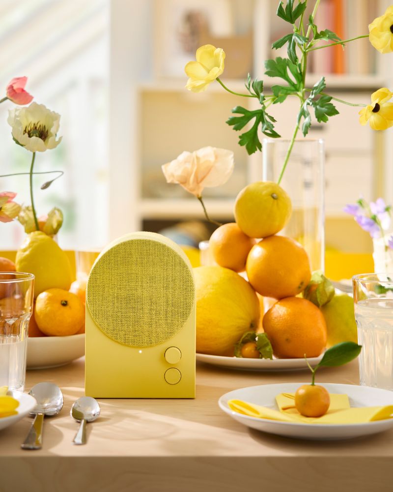 A yellow NATTBAD Bluetooth speaker is placed on a table that’s been decorated in yellow and orange for a festive party.