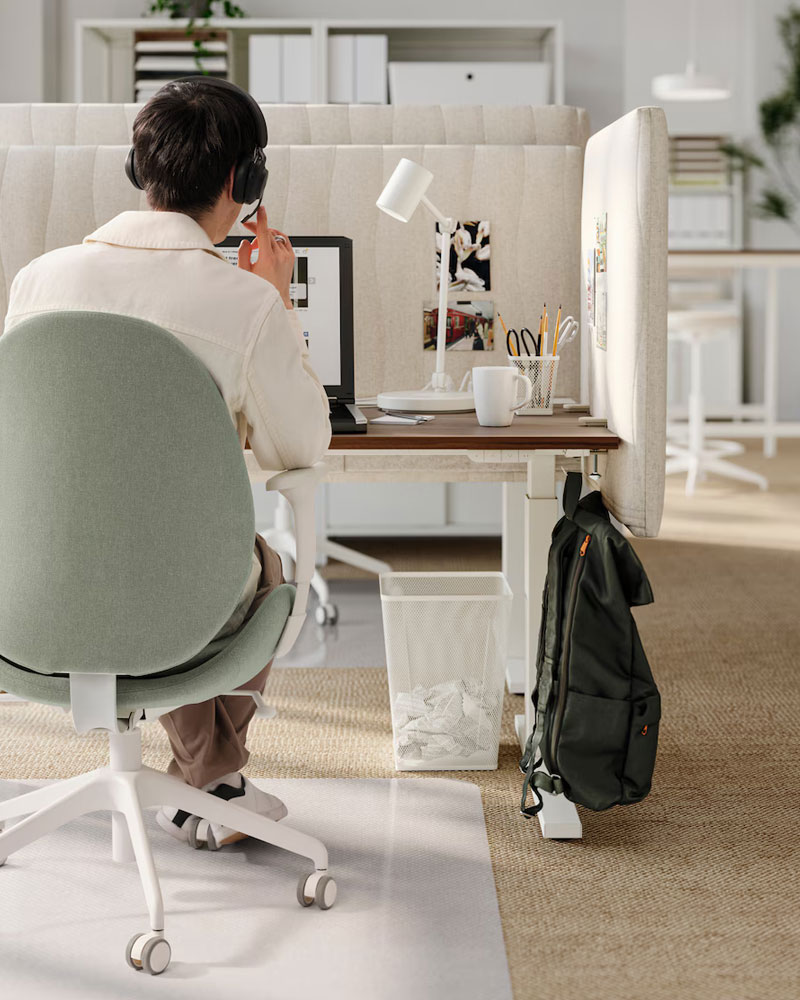 Back shot of a person sitting in a work chair in an office cubicle, even a floor protector for the chair wheels can be seen.
