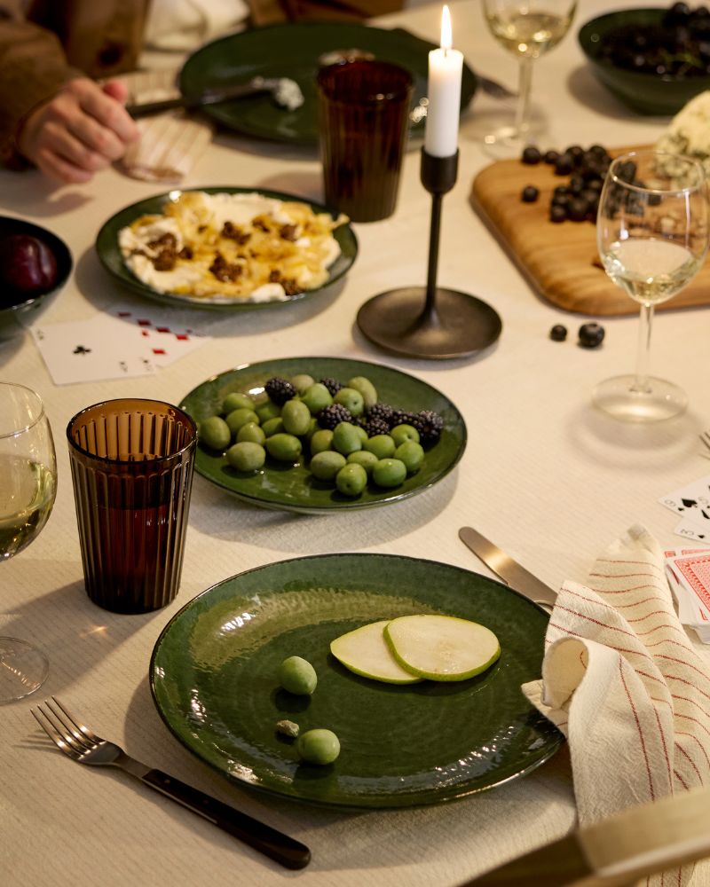 People are sitting around a festive table that’s set with wine glasses and green PELARKAKTUS plates, bowls and side plates.